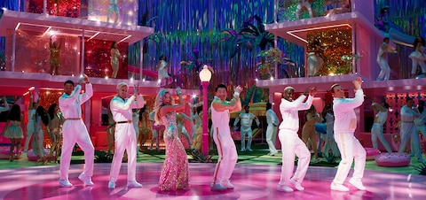 Barbie (Margot Robbie) and five Kens clap their hands above their head in a choreographed dance scene.