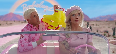 Ken (Ryan Gosling) shows off his neon yellow and pink inline skates to Barbie (Margot Robbie), who rolls her eyes as she drives them out of Barbieland in her pink convertible.
