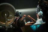 Behind the scenes, an actor lies in a bath as crew members add bubbles and Blitz Bazawule looks on.