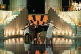 Celie, in a black beaded dress, and Shug, in a silver beaded dress, hold hands as they perform on stage with a full band and an elaborate, Art Deco-style set.