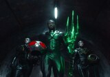 Black Manta walks down a tunnel holding the glowing Black Trident in his left hand and his helmet under his right arm. He is flanked by two henchmen.