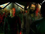 Orm and Aquaman stand in a red-lit, industrial space, looking at a helmeted figure in front of them.