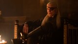 Prince Aemond Targaryen sits in an armchair with gilded details, his face illuminated by candlelight.