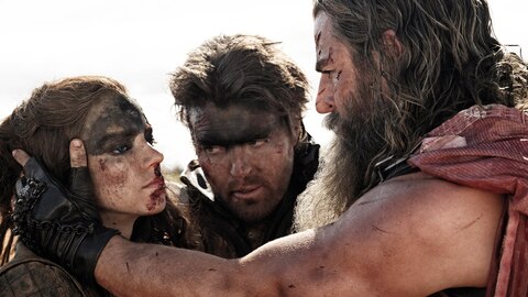 Dementus holds Furiosa’s head, looking closely at her face, as Praetorian Jack watches. 