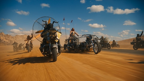 Dementus drives the chariot, a custom vehicle made up of three motorcycles and a chariot seat, through the Wasteland surrounded by members of the Biker Horde on motorcycles. 