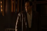 Oz Cobb stands in a dark room and looks at something out of frame.