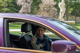 Victor Aguilar sits in the driver’s seat of a purple Maserati sedan and looks at something outside of the car with a concerned expression.