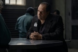 Oz Cobb sits at a metal table with a badge on his jacket lapel that reads “Blackgate Penitentiary, Visitor.”