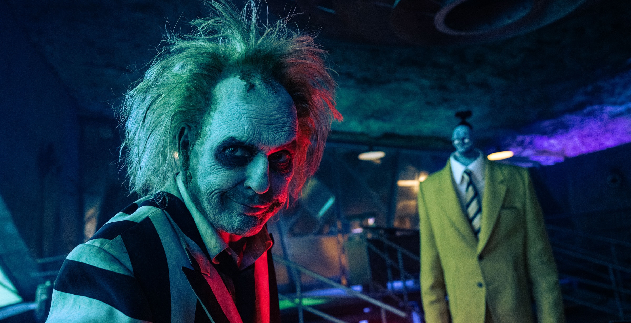 Beetlejuice looks at something out of frame. Bob (Shrinker) stands behind him.