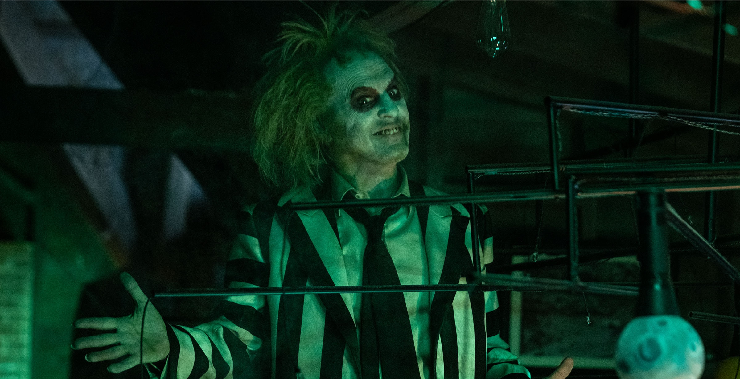 Beetlejuice stands in a dark room with his arms open and a smile on his face.