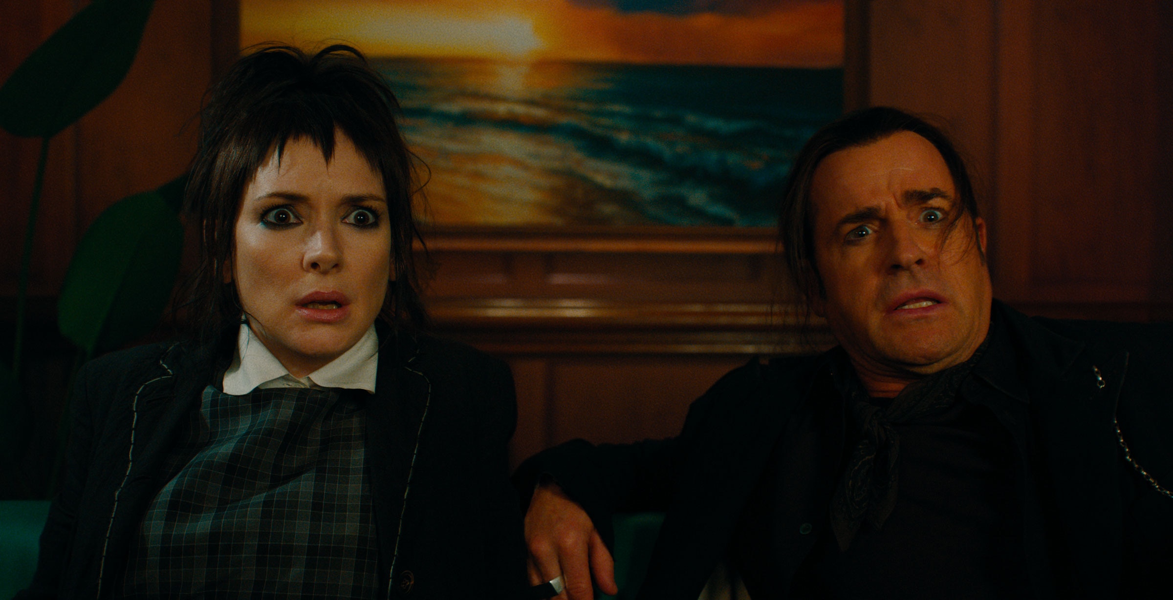 Lydia Deetz and Rory sit next to each other in a wood-paneled room and look alarmed by something out of frame.