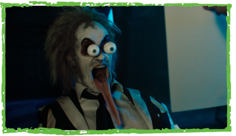 Beetlejuice cartoonishly screams with large bulging eyes, mouth wide open, and a ridiculously long tongue hanging out. ASL performer Sophia Morales stands in the bottom right and signs “screaming.”