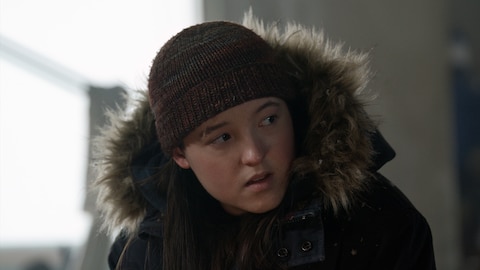 Close-up of Ellie in a parka and knit hat. She looks at something out of frame.