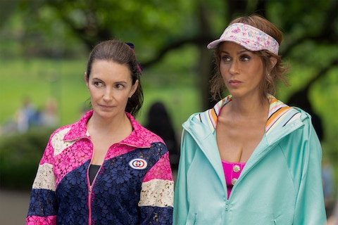 Charlotte and LTW look at something out of frame. Charlotte is wearing a pink, blue, and white jacket. LTW is dressed in a light green jacket and a floral-patterned visor.