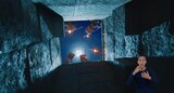 From the bottom of a stone shaft, we see five skeletons holding bows and flaming arrows and peering down menacingly. ASL interpreter Sophia Morales signs “screaming.”