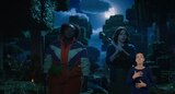 Dawn and Natalie walk through the woods at night. Dawn looks straight ahead calmly and holds a weapon down at her side. Natalie looks to her left with a worried expression and holds a weapon over her right shoulder with both hands. ASL interpreter Sophia Morales signs “breathing.”