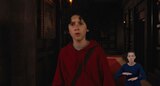 Henry stands in a dark hallway and looks at something out of frame with a concerned expression. ASL interpreter Sophia Morales signs “noise.”