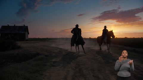 Two men shrouded in shadows ride horses down a dirt road as the sun sets. There is a large building in the background. BASL interpreter Nakia Smith signs “go.”