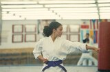 Willa, wearing a white karate uniform with a purple belt, stands in a brightly lit martial arts studio with her left “primary” hand extended and her right “hikite” hand pulled back to her hip.