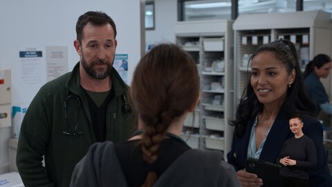 In a medical supply area, Dr. Robby and Nurse Noelle Hastings are engaged in a conversation with Dr. McKay, whose back is to the camera. On the right side of the image, ASL performer Amelia Hensley signs "neutral." 