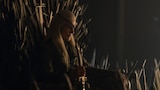 Aemond Targaryen is seen in profile, sitting on the Iron Throne with his right hand holding the hilt of a longsword. He stares ahead at something out of frame.