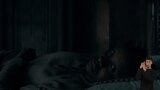 A dimly lit bedroom. Grand Maester Orwyle lies awake in bed, resting his head on a pillow while looking out into the darkness. In the bottom right side of the image, ASL dubber Landen Gonzales signs "Knocking on the door."