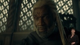 Close-up of Lord Corlys Velaryon, seated with a wooden screen behind him. He looks down at something out of frame. ASL dubber Landen Gonzales signs “Really.”